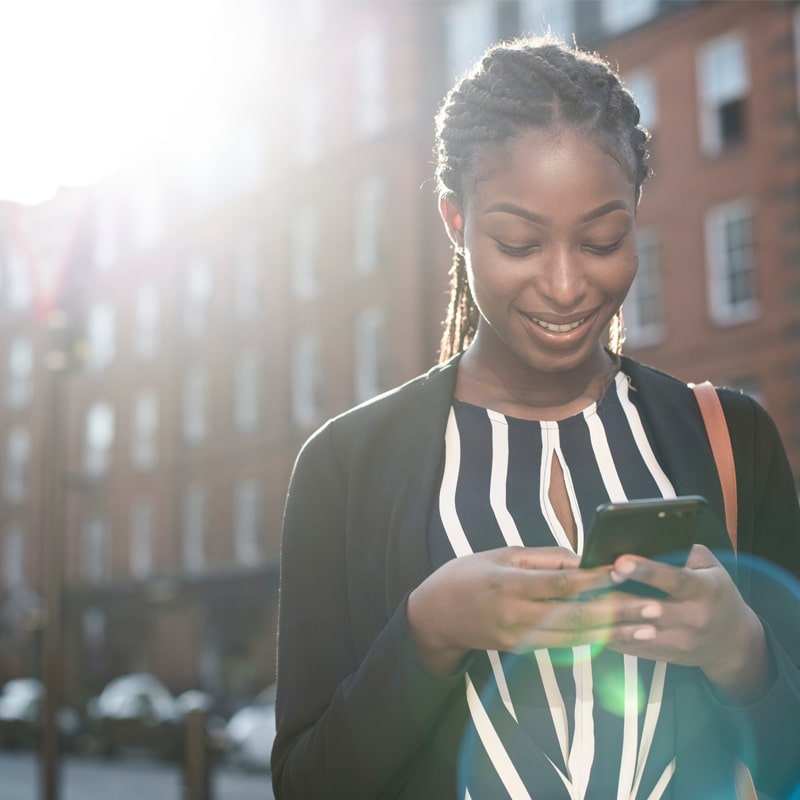 African American woman smiling at her phone with sun flare